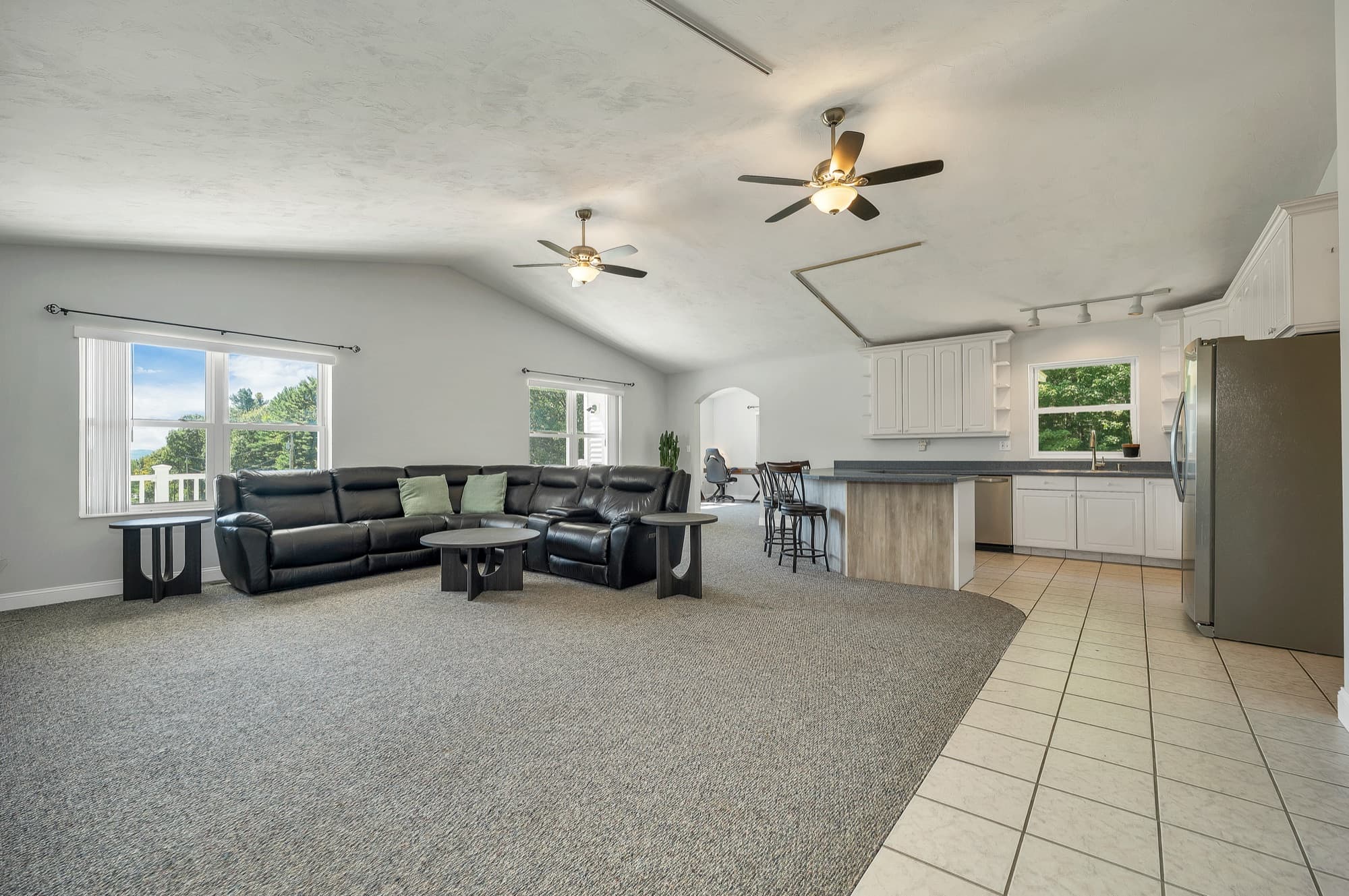 The vaulted family room with the sectional, a ceiling fan, and the kitchen beyond