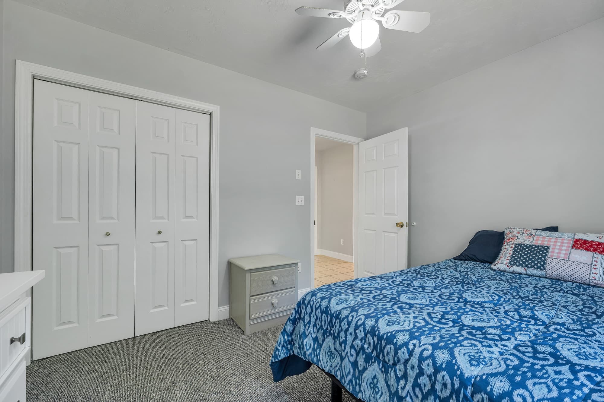A bedroom with a double closet, carpet, and a ceiling fan
