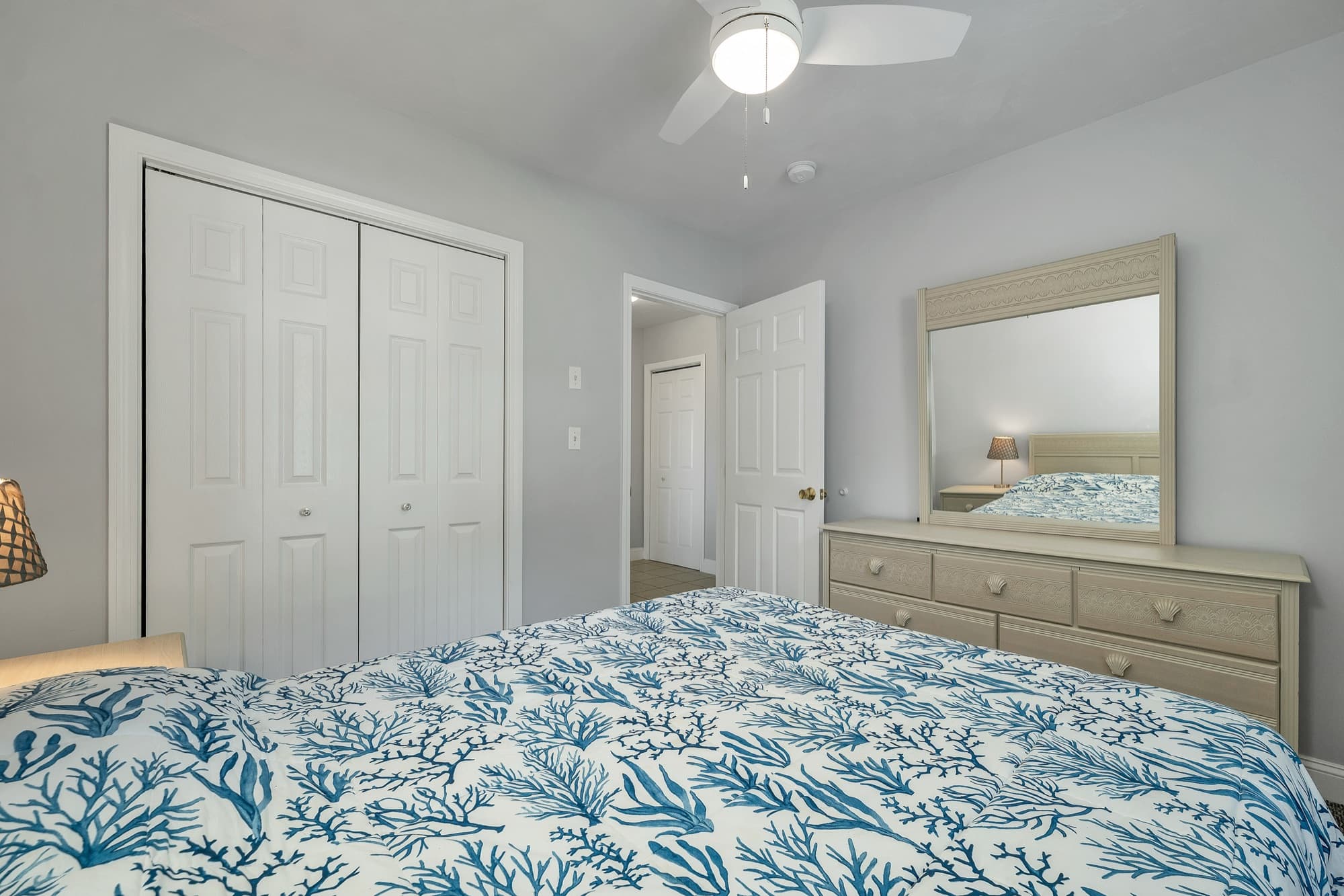 A bedroom with a double closet, a dresser, and a ceiling fan